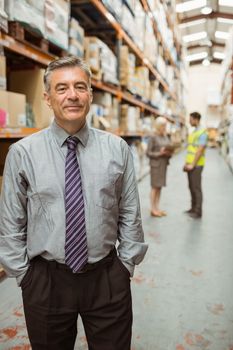 Cheerful businessman with hands in pocket posing in a large warehouse