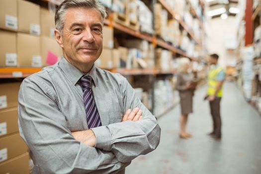 Smiling businessman with crossed arms in a large warehouse