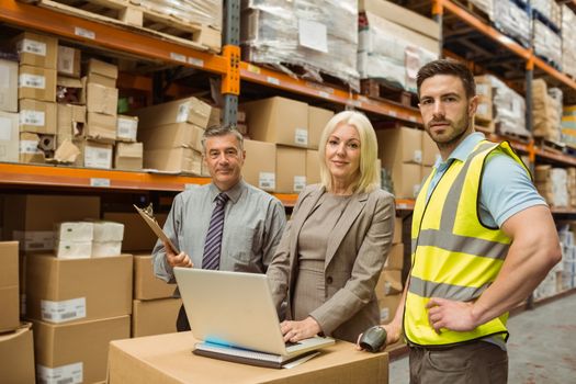 Smiling warehouse team working together on laptop in a large warehouse