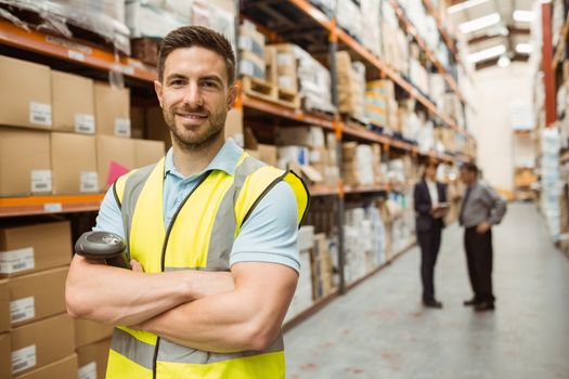 Smiling worker standing with arms crossed in a large warehouse