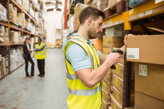 Warehouse worker scanning barcode on box in a large warehouse