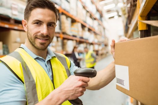 Warehouse worker scanning box while smiling at camera in a large warehouse