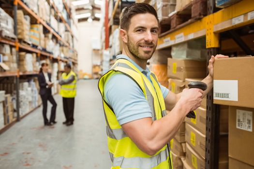 Warehouse worker scanning box while smiling at camera in a large warehouse