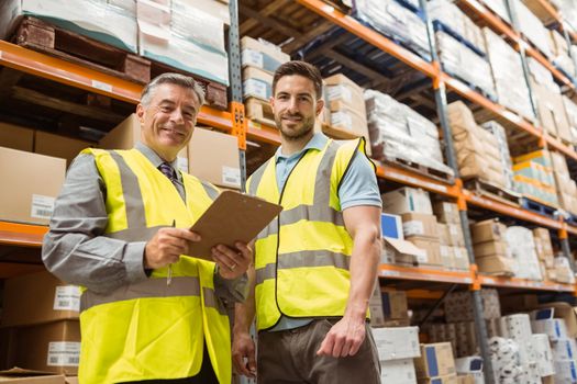 Warehouse manager and foreman looking at camera in a large warehouse