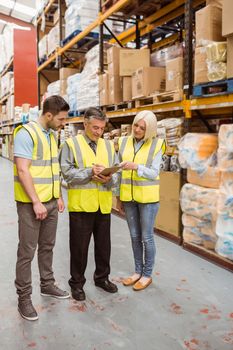 Manager writing on clipboard talking to colleague in a large warehouse