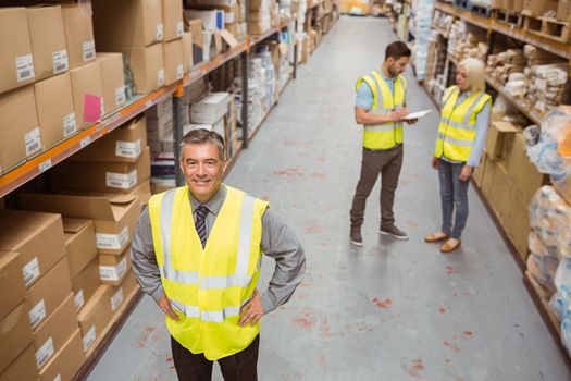 Smiling manager placing his hands on his hips in a large warehouse