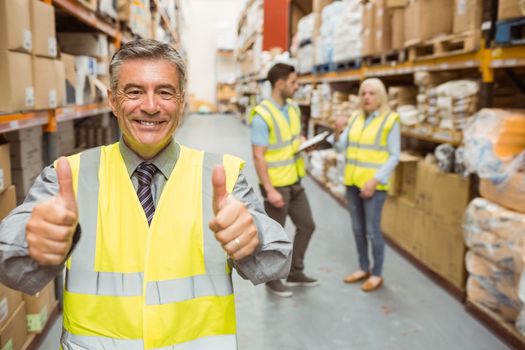 Manager smiling at camera showing thumbs up in a large warehouse