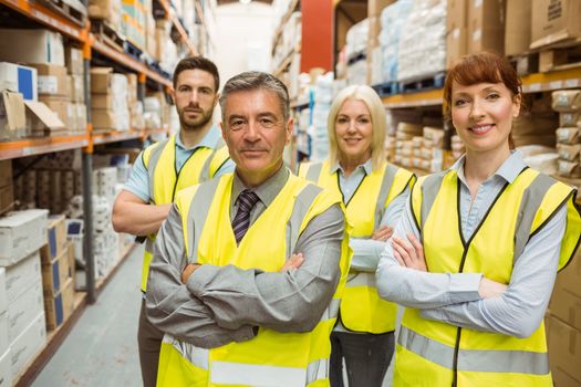 Smiling warehouse team with arms crossed in a large warehouse