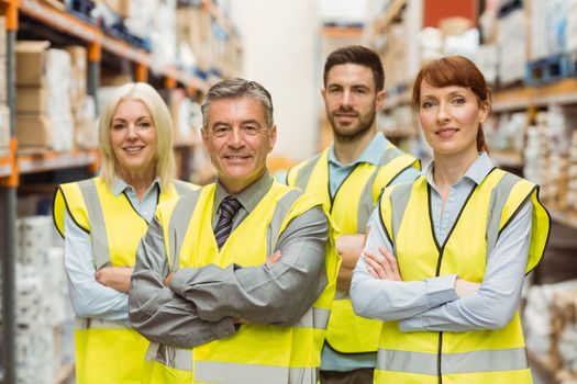 Smiling warehouse team with arms crossed in a large warehouse