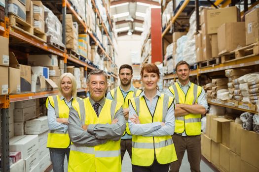 Smiling warehouse team with arms crossed in a large warehouse