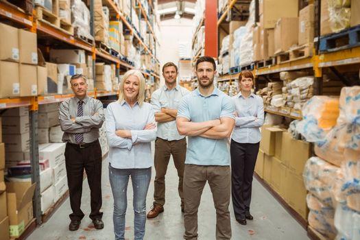 Smiling warehouse team with arms crossed in a large warehouse