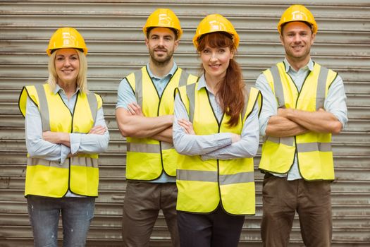 Warehouse team with arms crossed wearing hard hat in a large warehouse
