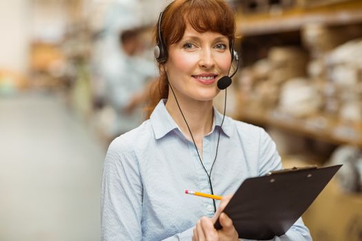 Warehouse manager writing on clipboard in a large warehouse