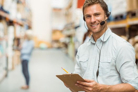 Warehouse manager wearing headset writing on clipboard in a large warehouse