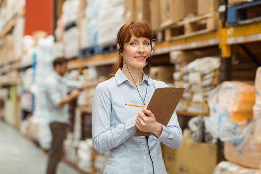 Warehouse manager writing on clipboard in a large warehouse