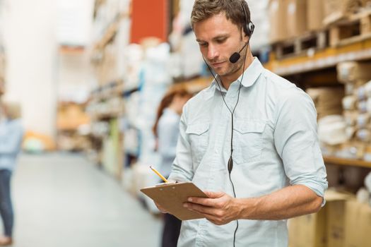 Warehouse manager wearing headset writing on clipboard  in a large warehouse