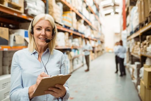 Smiling warehouse manager writing on clipboard in a large warehouse