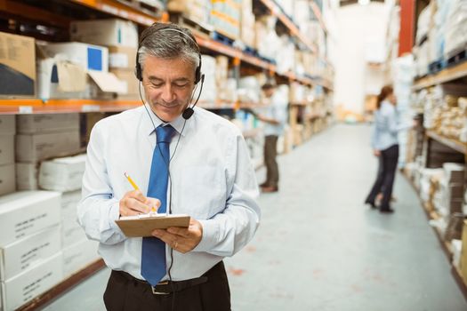 Smiling warehouse manager writing on clipboard in a large warehouse