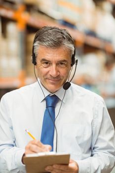 Smiling warehouse manager writing on clipboard in a large warehouse