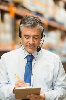 Smiling warehouse manager writing on clipboard in a large warehouse