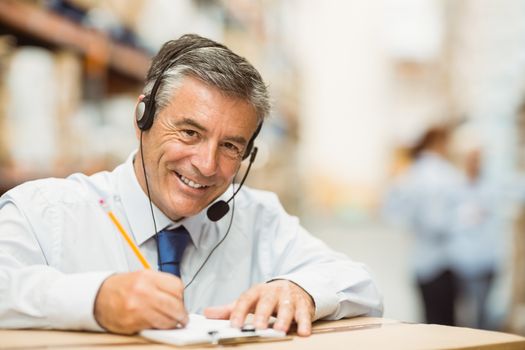 Smiling warehouse manager writing on clipboard in a large warehouse