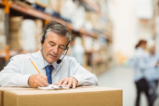 Warehouse manager writing on clipboard in a large warehouse