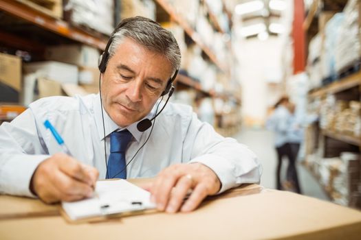 Warehouse manager writing on clipboard in a large warehouse