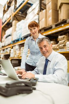 Warehouse management talking and looking at laptop in a large warehouse