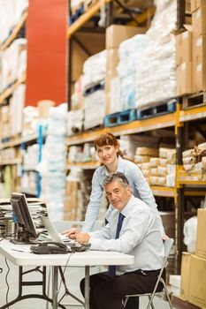 Warehouse managers working together on laptop in a large warehouse