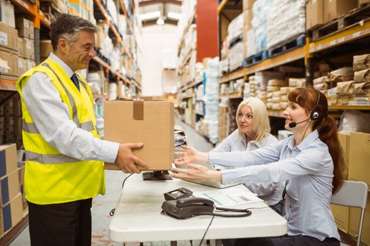 Manager wearing yellow vest giving box to his colleague in a large warehouse