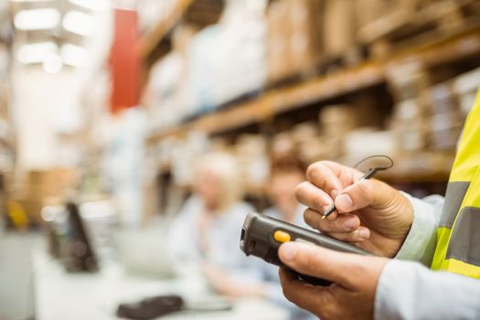 Close up of manager wearing yellow vest using handheld in a large warehouse