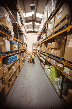 Worker with trolley of boxes in a large warehouse