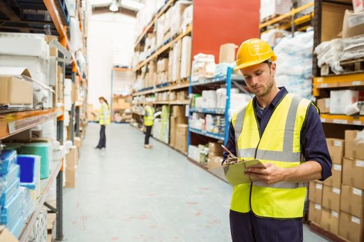 Focused warehouse worker with clipboard in a large warehouse