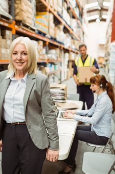 Smiling warehouse manager leaning on desk in a large warehouse