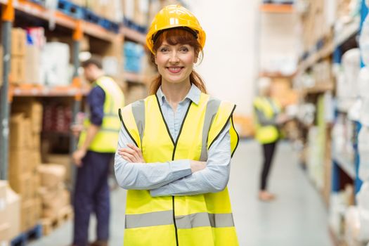 Warehouse manager smiling at camera with arms crossed in a large warehouse