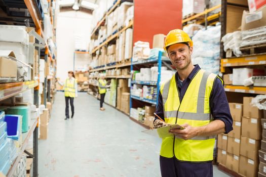 Warehouse worker smiling at camera with clipboard in a large warehouse