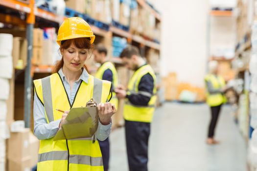 Pretty warehouse manager writing on clipboard in a large warehouse