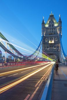 Tower Bridge in London, UK at night with moving red double-decker bus leaving light traces