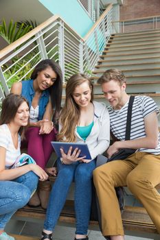 Smiling students sitting on steps with tablet pc at the university
