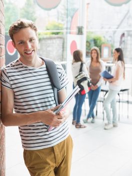 Handsome student smiling and holding notepads at the university