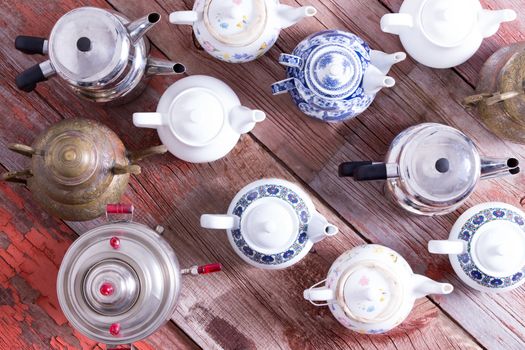 Army of a assorted metal and ceramic Turkish and conventional tea pots arranged in regimental rows all facing the same direction viewed from above on a rustic wood background