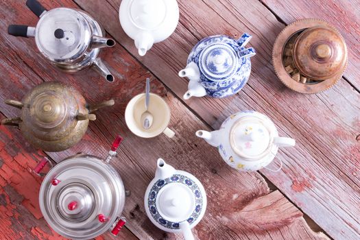 Tea on demand concept with a radiating circle of teapots arranged with their spouts facing a central empty cup and teaspoon on a rustic wooden table, overhead view