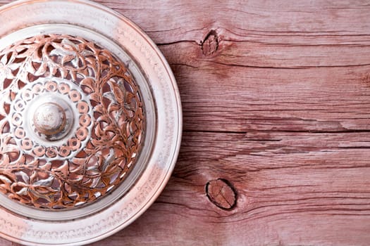 Old rustic metal plate with an ornate perforated cover on the left side on a rustic wooden table with copyspace