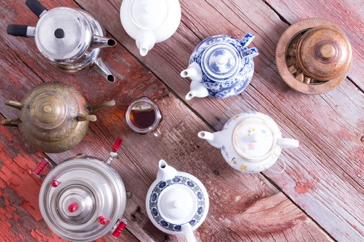 Easy tea from a teabag versus quality brewed tea from a tea pot in a conceptual image with a central cup of tea surrounded by a circle of different teapots on a rustic wooden table, viewed from above