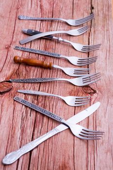 Array of rustic forks and a single knife arranged randomly in a receding row on a rustic wooden table in a conceptual image