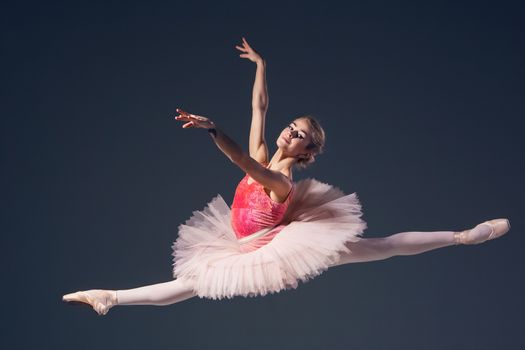 Beautiful female ballet dancer on a grey background. Ballerina is wearing  pink tutu and pointe shoes