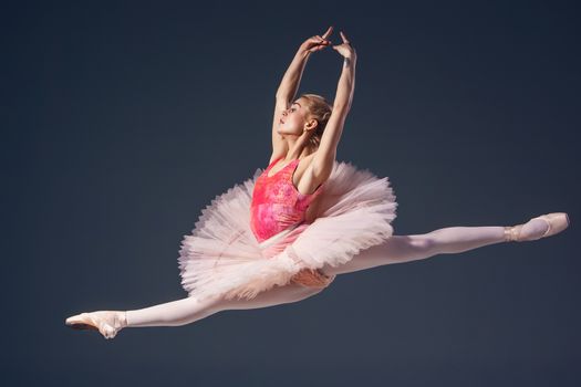 Beautiful female ballet dancer on a grey background. Ballerina is wearing  pink tutu and pointe shoes