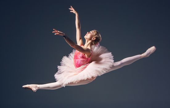 Beautiful female ballet dancer on a grey background. Ballerina is wearing  pink tutu and pointe shoes