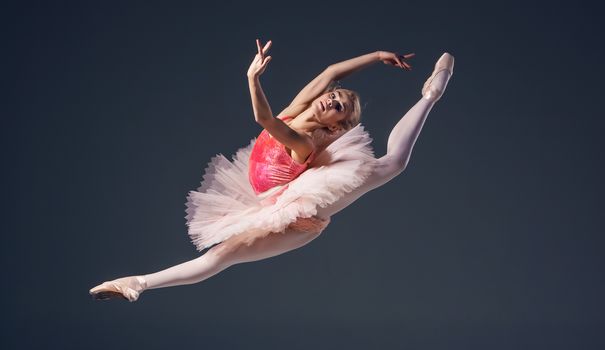 Beautiful female ballet dancer on a grey background. Ballerina is wearing  pink tutu and pointe shoes