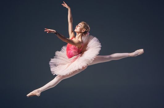 Beautiful female ballet dancer on a grey background. Ballerina is wearing  pink tutu and pointe shoes